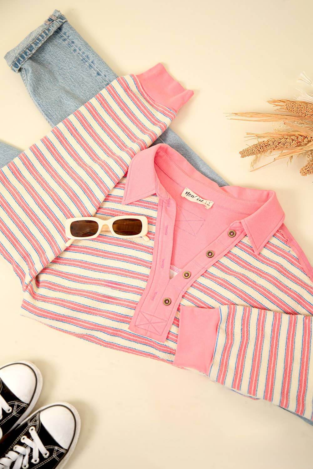 Oversized casual striped knit top in pink and blue, styled with denim, sunglasses, and sneakers for an early fall look.