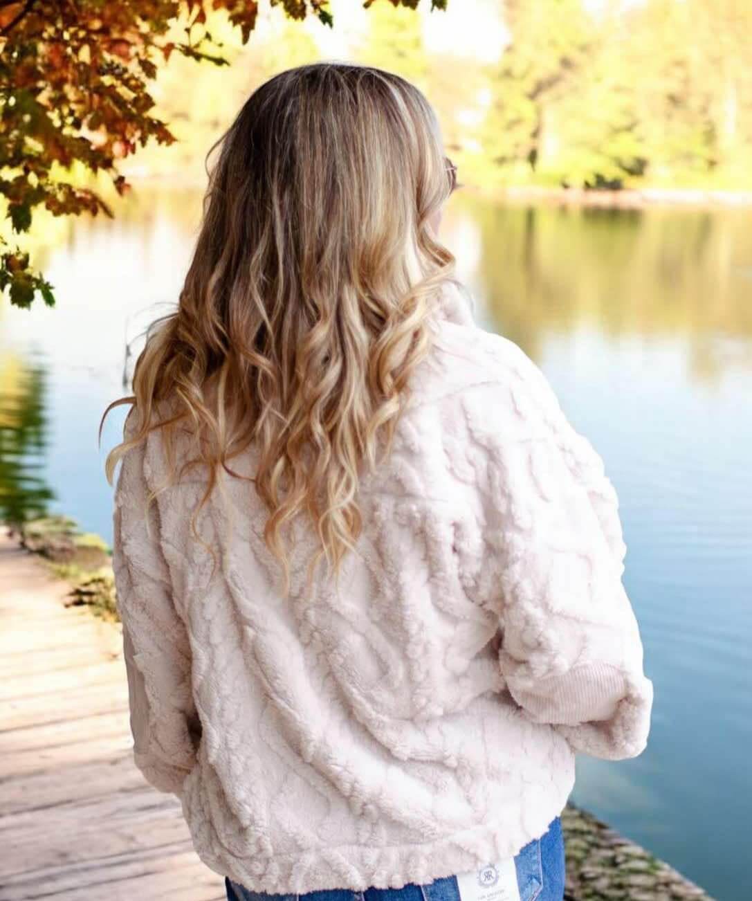 Woman wearing ivory teddy bear sherpa pullover with cable pattern, standing by a lake in autumn.