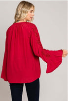 Woman wearing red Rayon blend top from Cotton Blue with bell sleeves and eyelet detailing, showcasing back view.