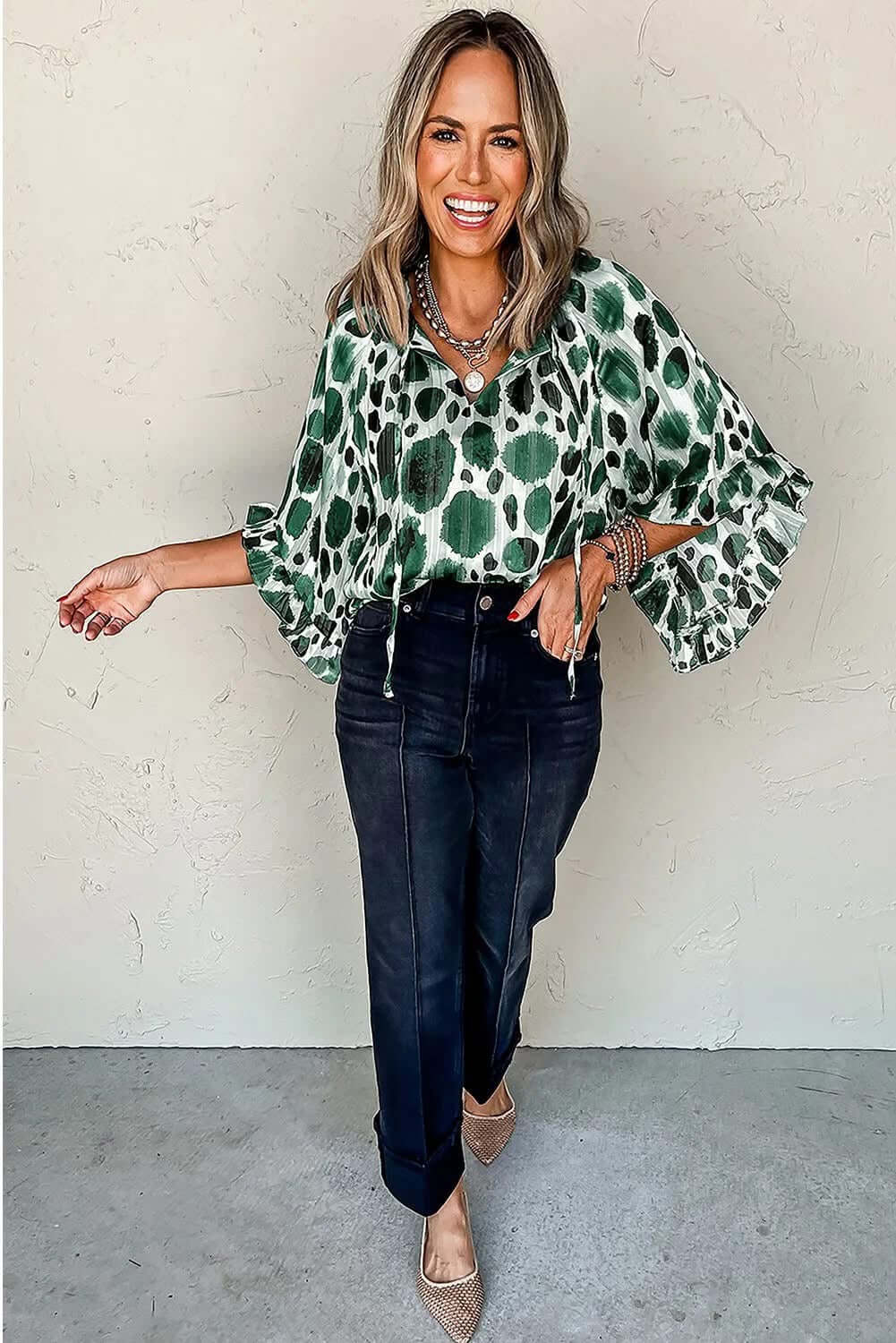 Woman smiling in the Enchanted Valley blouse with ruffled sleeves and spotted design, paired with black jeans.