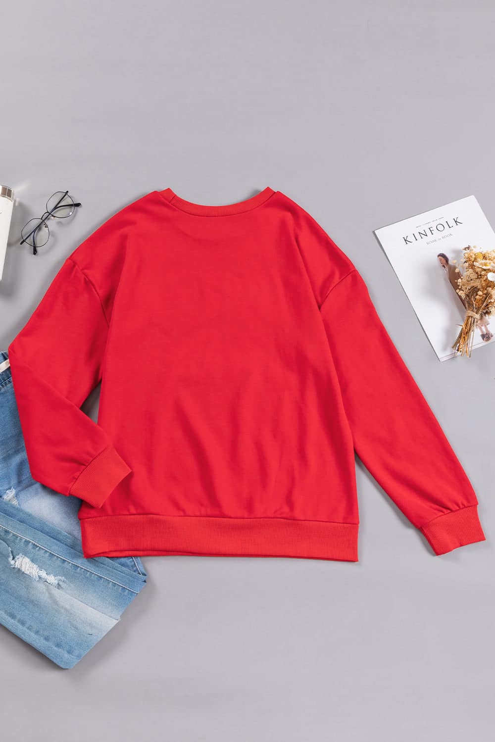 Red crewneck sweatshirt with long sleeves, styled with blue jeans and paired with trendy glasses and Kinfolk magazine.