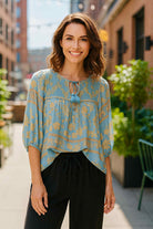 Model wearing TUSCAN DREAM Top - UMGEE, featuring a blue and golden floral pattern with smocked neckline and tassel ties.