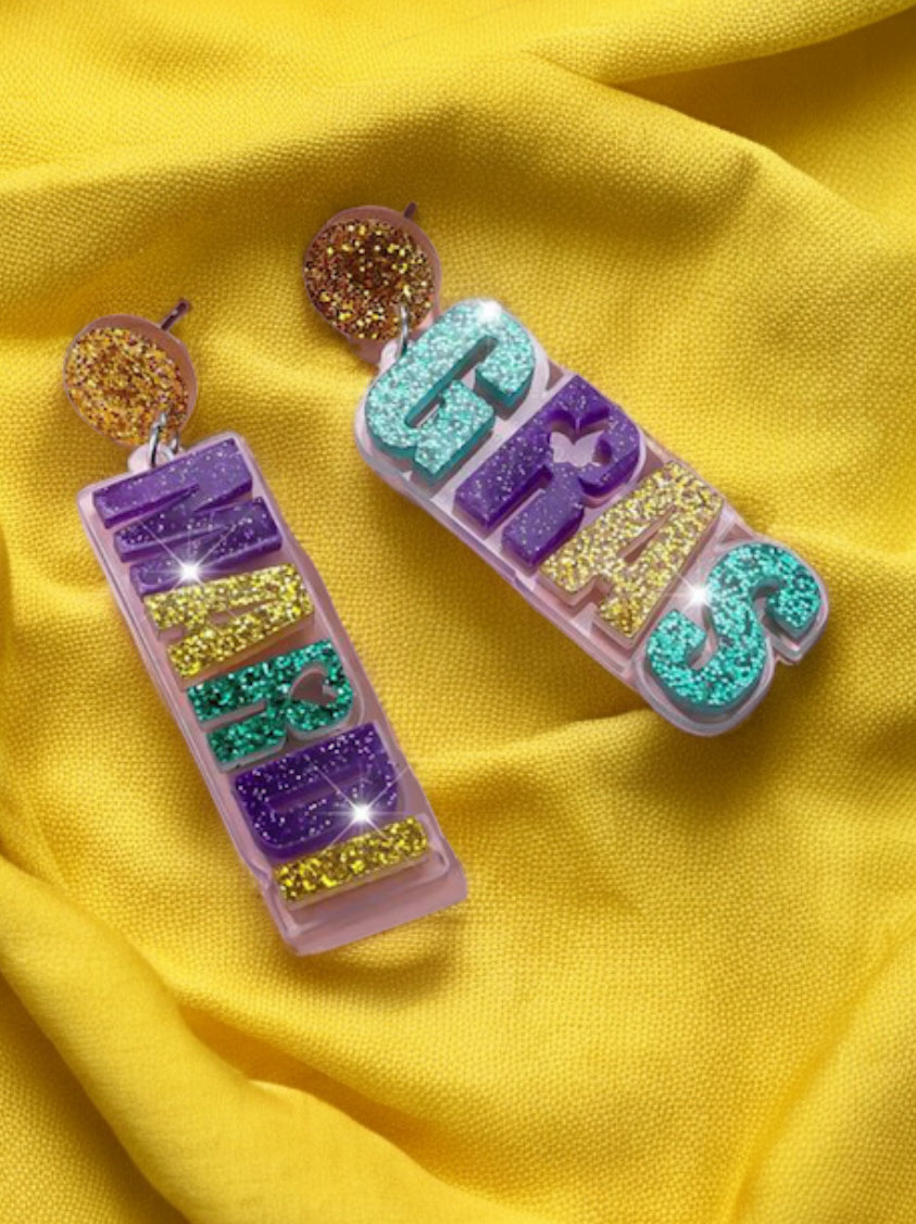 Mardi Gras ear adornments featuring colorful glitter letters on a yellow background.