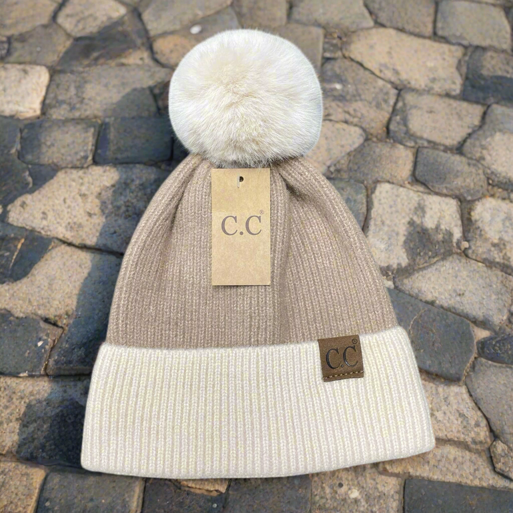 Tan OH SO SOFT BEANIE by C.C. with luxurious fur pom pom and beige cuff featuring suede patch, showcased on textured background.