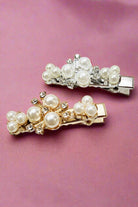 Set of two pearl accent hair clips in gold and silver, featuring clusters of pearls and rhinestones, resting on a surface.