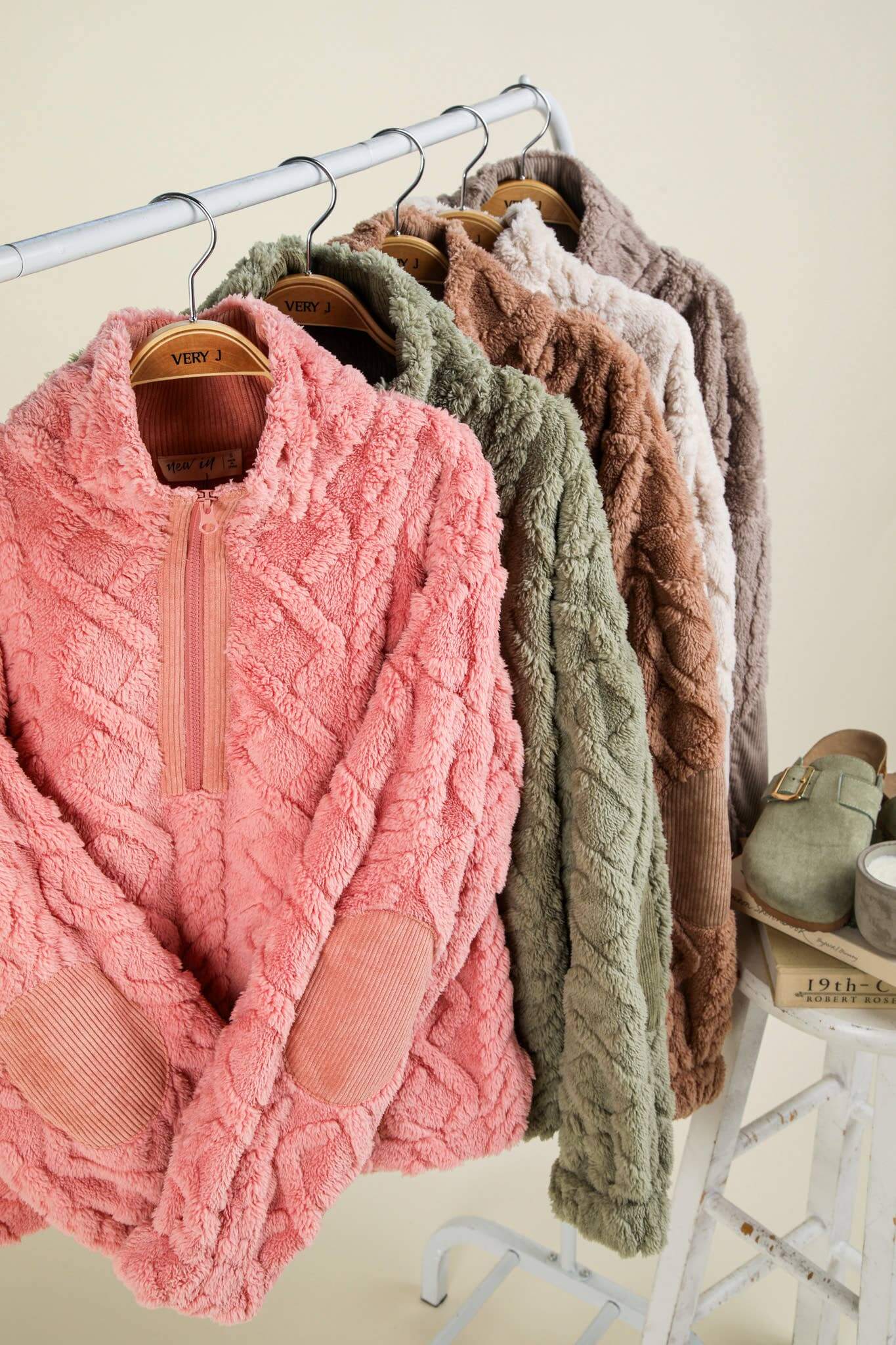 Cozy cable patterned fleece pullovers in various colors on hangers, featuring elbow corduroy patches and half zip design.