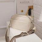 Beige SAMANTHA Crossbody Bag with Montana West strap on white table, featuring sleek PU leather design and adjustable strap.