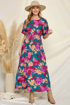 Floral maxi dress with vibrant colors, model wearing a hat, perfect for summer outings and special occasions.