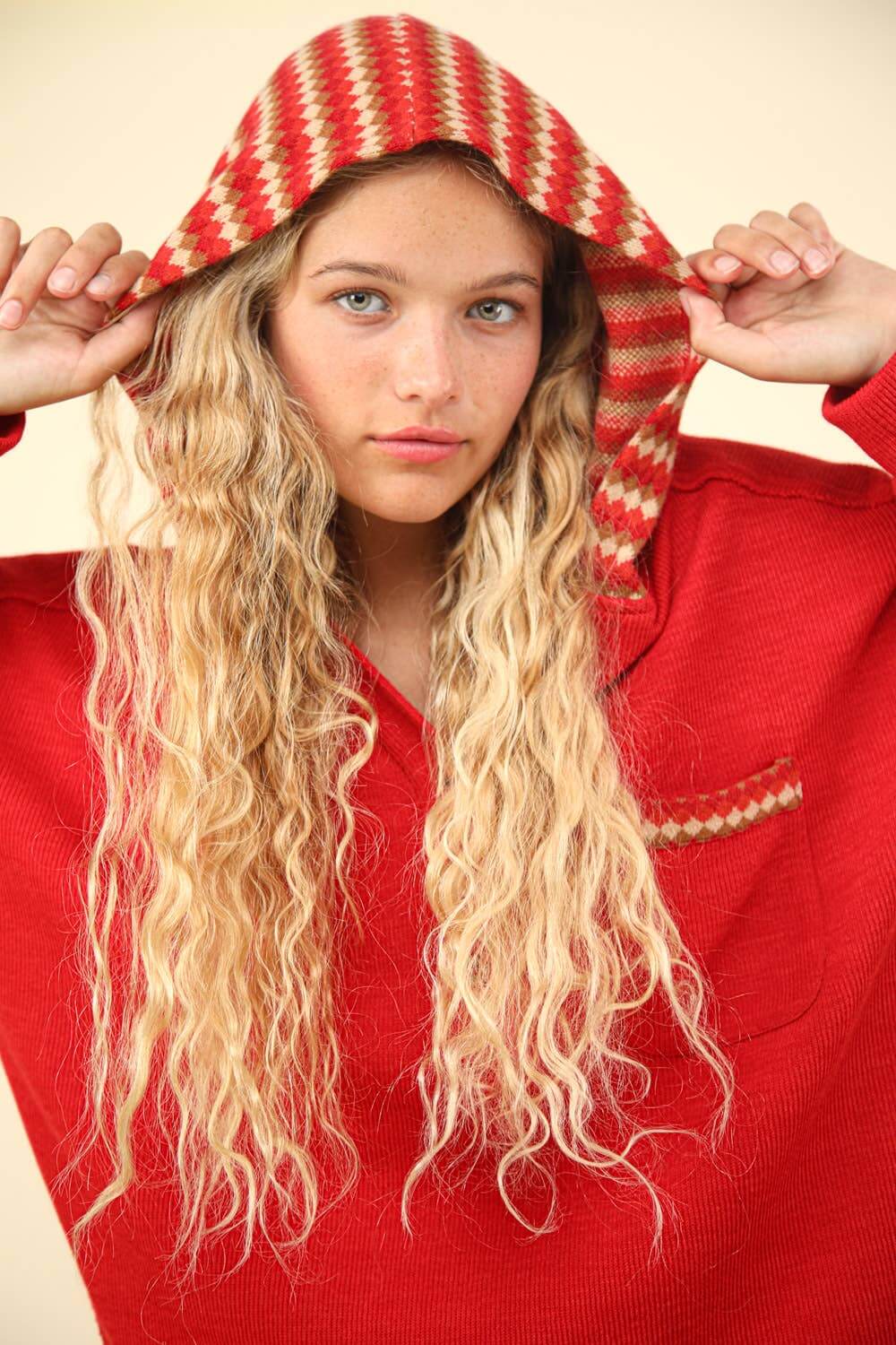 Model wearing red oversized contrast hoodie with patterned hood, showcasing long curly hair and relaxed style.