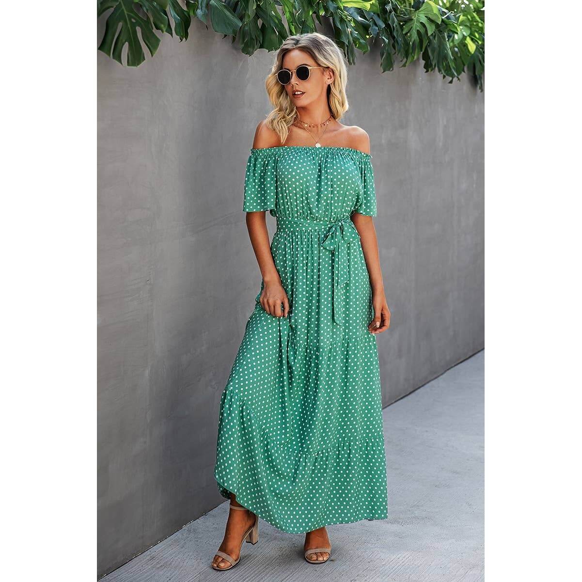 Model wearing an off-shoulder green polka dot maxi dress with short sleeves and waist tie, suitable for casual outings.