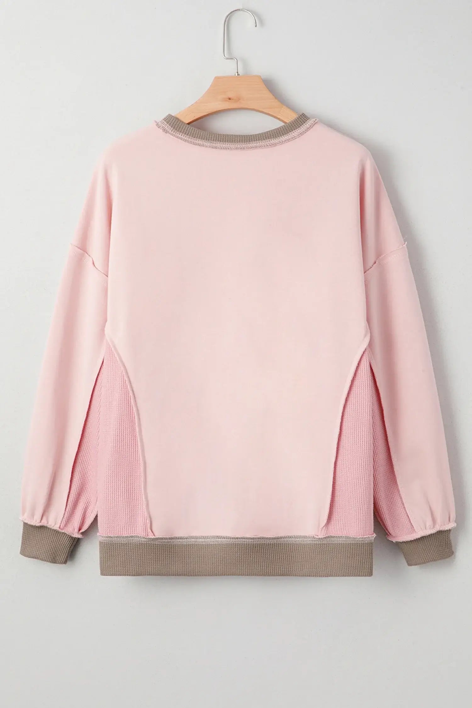 Back view of the FROM THE HEART PULLOVER featuring a soft light pink color, trendy exposed seams, and waffle-textured patchwork.