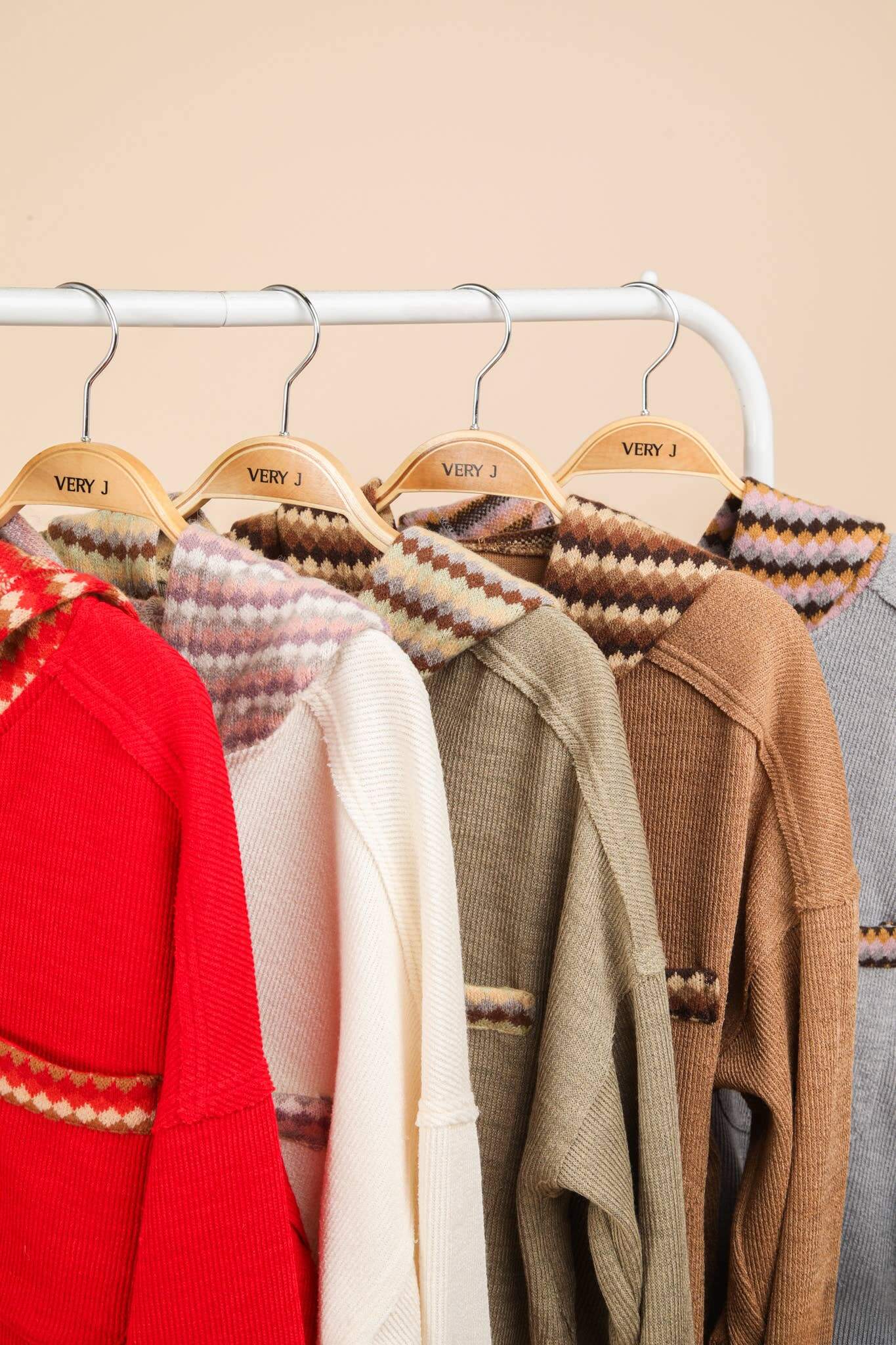 Various oversized contrast hoodies in red, white, green, brown, and gray hanging on a rack with 'Very J' labels.