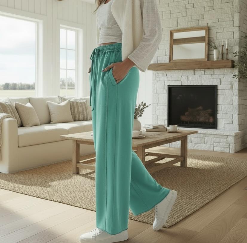 A person wearing AQUA DRIFT WIDE LEG PANTS in a cozy living room with a fireplace.