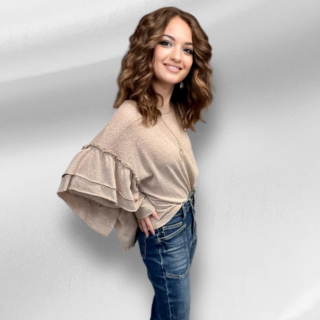 Woman wearing Soft Landing Top in neutral tan with double ruffle detail and mineral wash finish, styled with jeans.