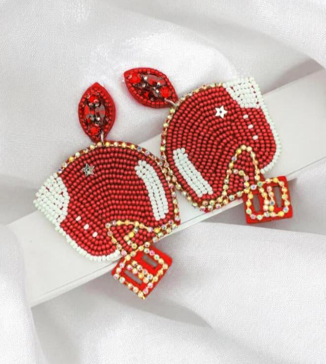 Red and white football helmet earrings with beaded design on a white fabric background.