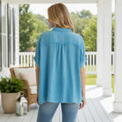 Back view of the CALMING COAST TOP - Umgee in light blue cotton gauze, showcasing its relaxed silhouette on a porch.