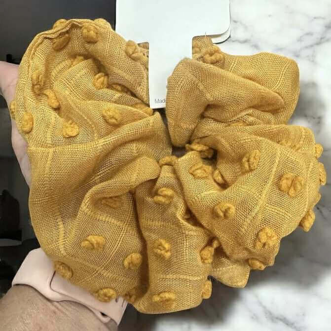 Cloud Comfort Scunchie in mustard yellow with pompom texture, perfect for stylish hair ties or wrist accessories.