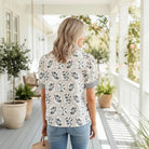 Woman wearing the CHOOSE JOY TOP with floral prints, puff sleeves, and a ruffled neckline, standing on a porch.