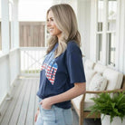 LULU MAC ALL AMERICAN COMFORT COLOR TEE model wearing navy tee with flag graphic, showcasing patriotic style.