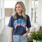 LULU MAC ALL AMERICAN COMFORT COLOR TEE worn by a smiling woman, featuring navy color and flag graphic design.