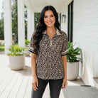 Woman wearing the NATURAL EDGE TOP in leopard print, styled casually on a porch surrounded by plants.