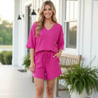 CONFIDENT COMFORT SHORTS SET in rich pink worn by a woman standing outside, showcasing a relaxed and modern style.