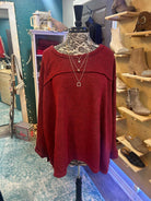 Dark red long-sleeve sweater with exposed seams, displayed on a mannequin in a boutique setting. Plus size availability.