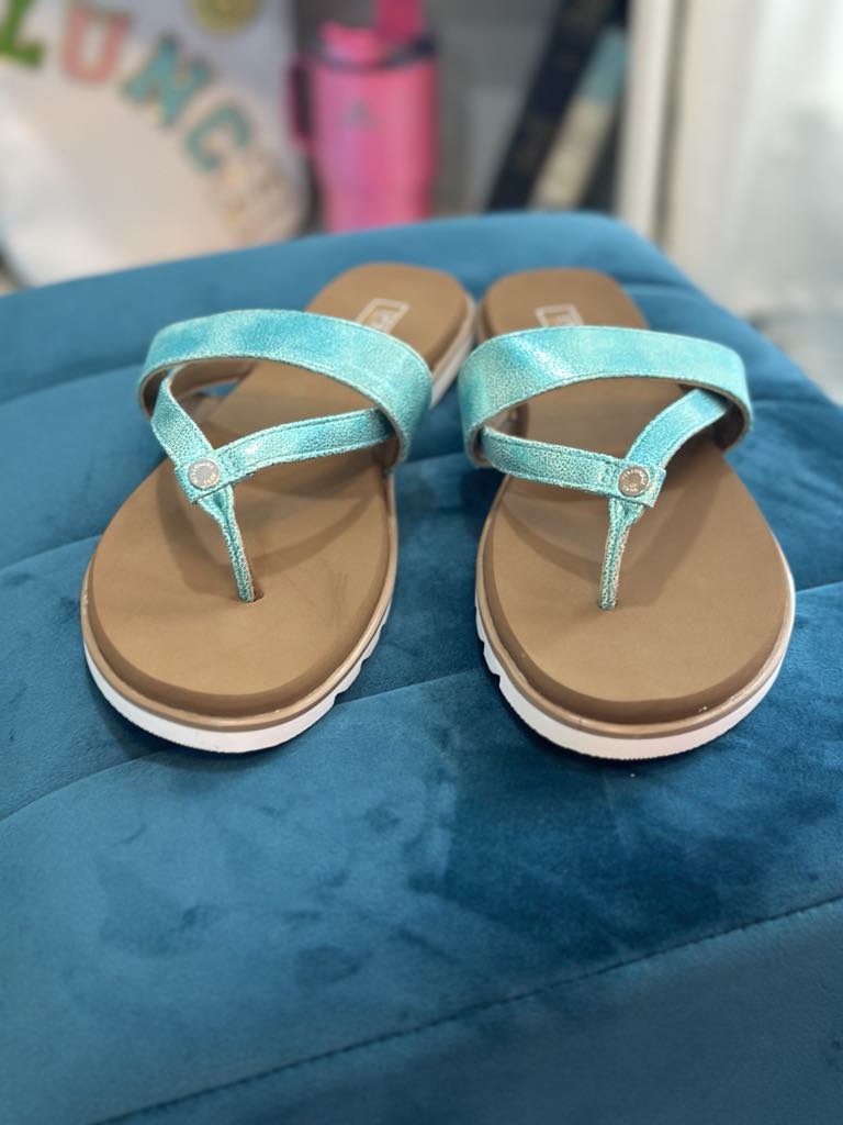 YELLOW BOX - SHAYNE turquoise flip flops with shimmer straps on a teal ottoman.