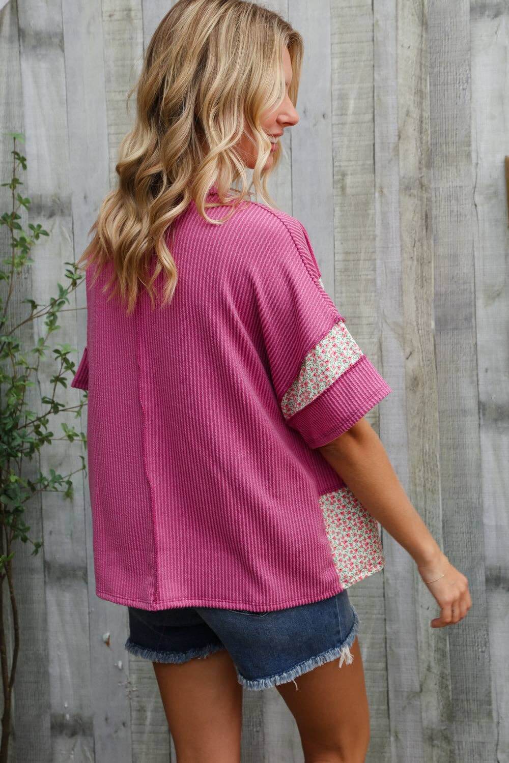 Model wearing a fuchsia floral color block pullover with wavy rib details over denim shorts.