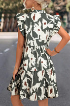 Woman wearing a forest-green floral flutter-sleeve mini dress, showcasing a stylish back view outdoors.
