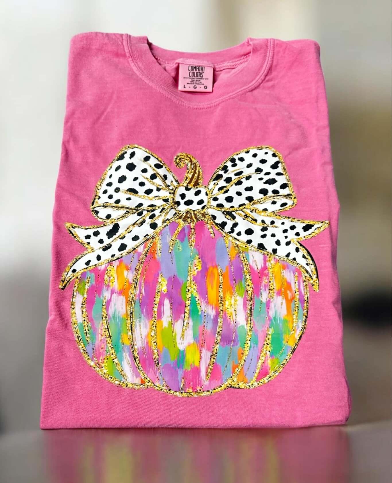 Pink Comfort Color tee with vibrant pumpkin applique featuring multicolor design and polka dot bow, 100% cotton, short-sleeved.