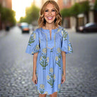 Model wearing the Blue Sky Beauty Dress with floral embroidery on a cobblestone street.