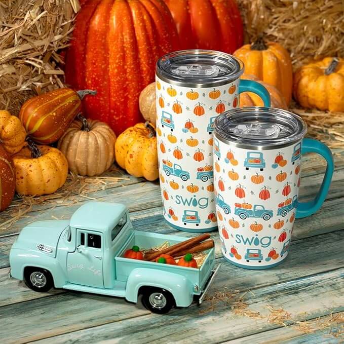 Two insulated pumpkin patch tumblers next to a vintage truck and pumpkins, perfect for fall beverages.