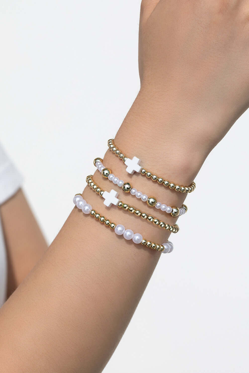 Timeless Faith bracelet stack featuring gold-tone beads, faux pearls, and white crosses on a wrist.