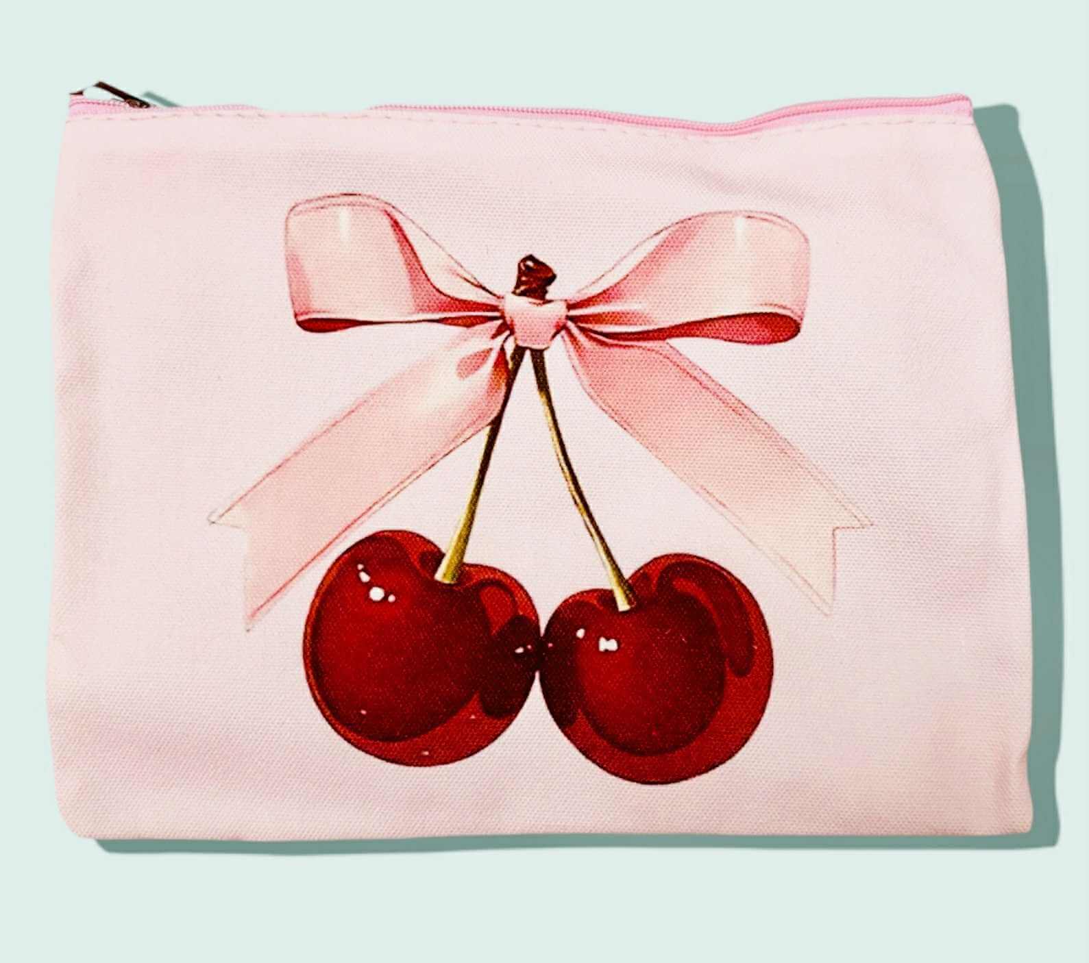 Pink cosmetic bag featuring two glossy cherries tied with a pink ribbon for a cute and stylish look.
