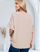 Back view of a woman wearing the Driftwood Sands top by Zenana, showcasing its sandy beige color and ruffled sleeves.