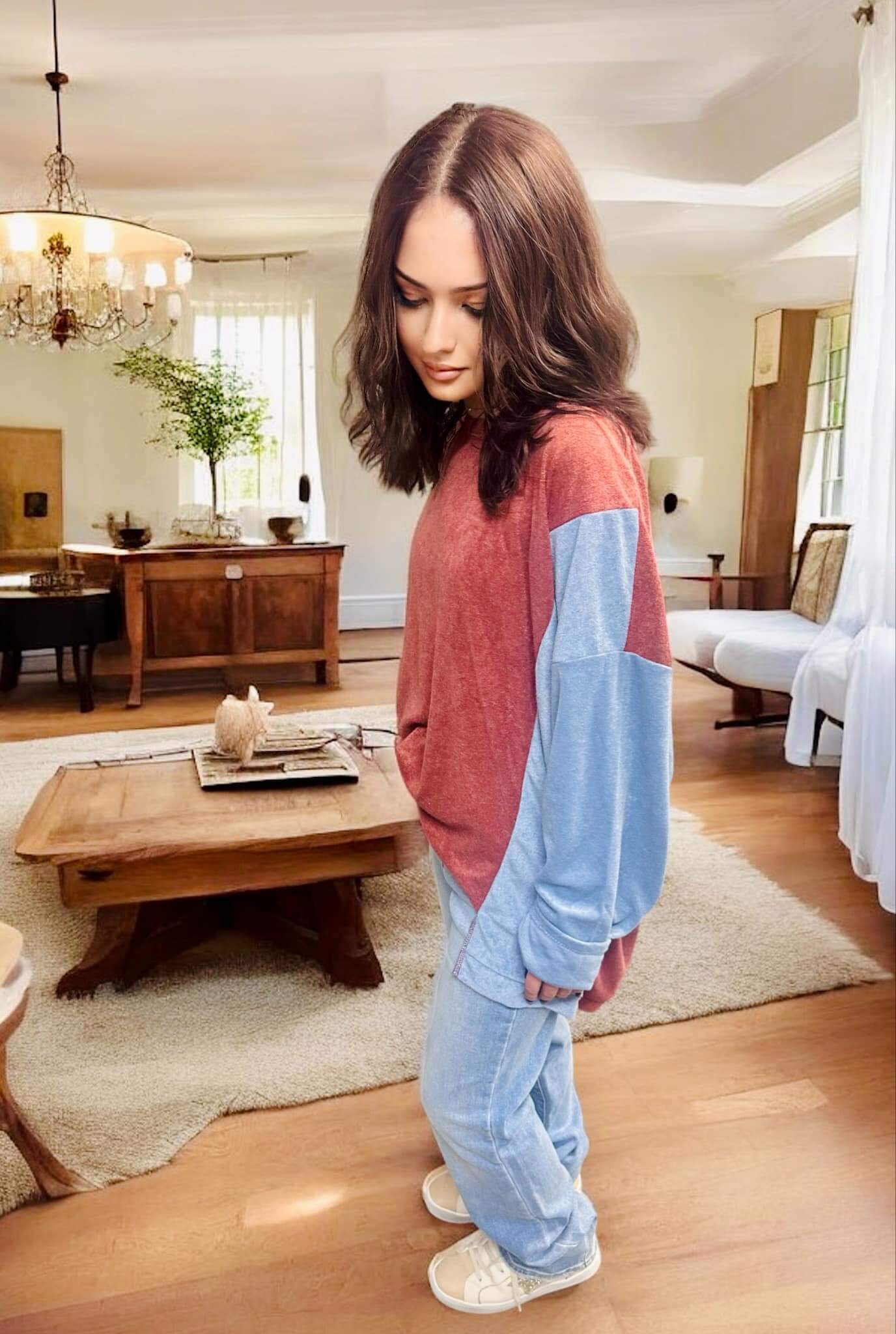 Woman wearing a TRAVELING LIGHT top by BiBi, showcasing burgundy and blue color block design, in a cozy living room setting.