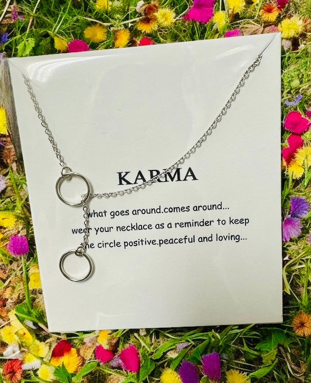 Silver-toned karma necklace featuring interlocking rings with an uplifting quote on a floral background.