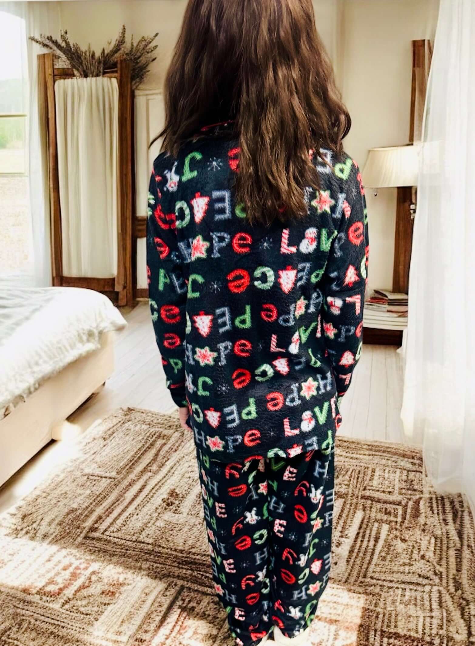 Woman wearing PEACE LOVE HOPE PJs with festive Christmas design and red trim in a cozy bedroom setting