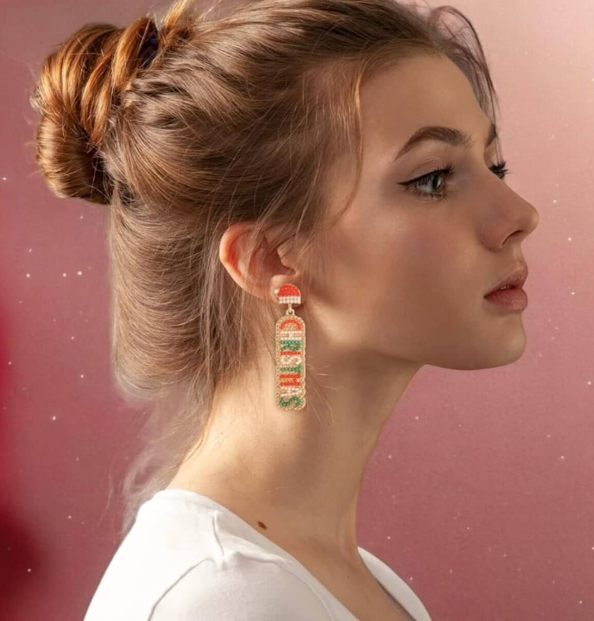 Side view of a woman wearing Merry Christmas Santa earrings with red, white, and green beads on a pink background.