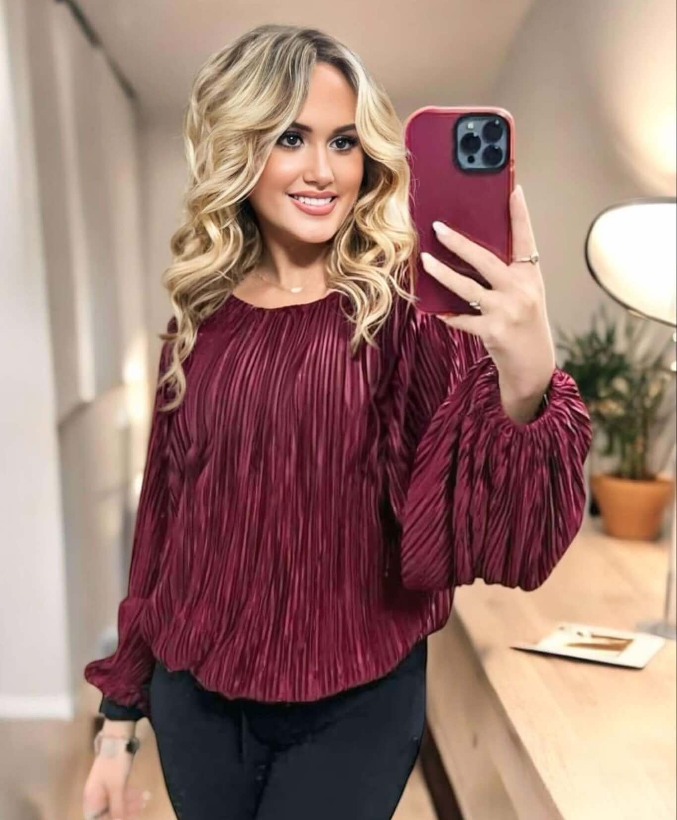 Woman wearing a dark burgundy pleated blouse with balloon sleeves taking a selfie in a modern room.