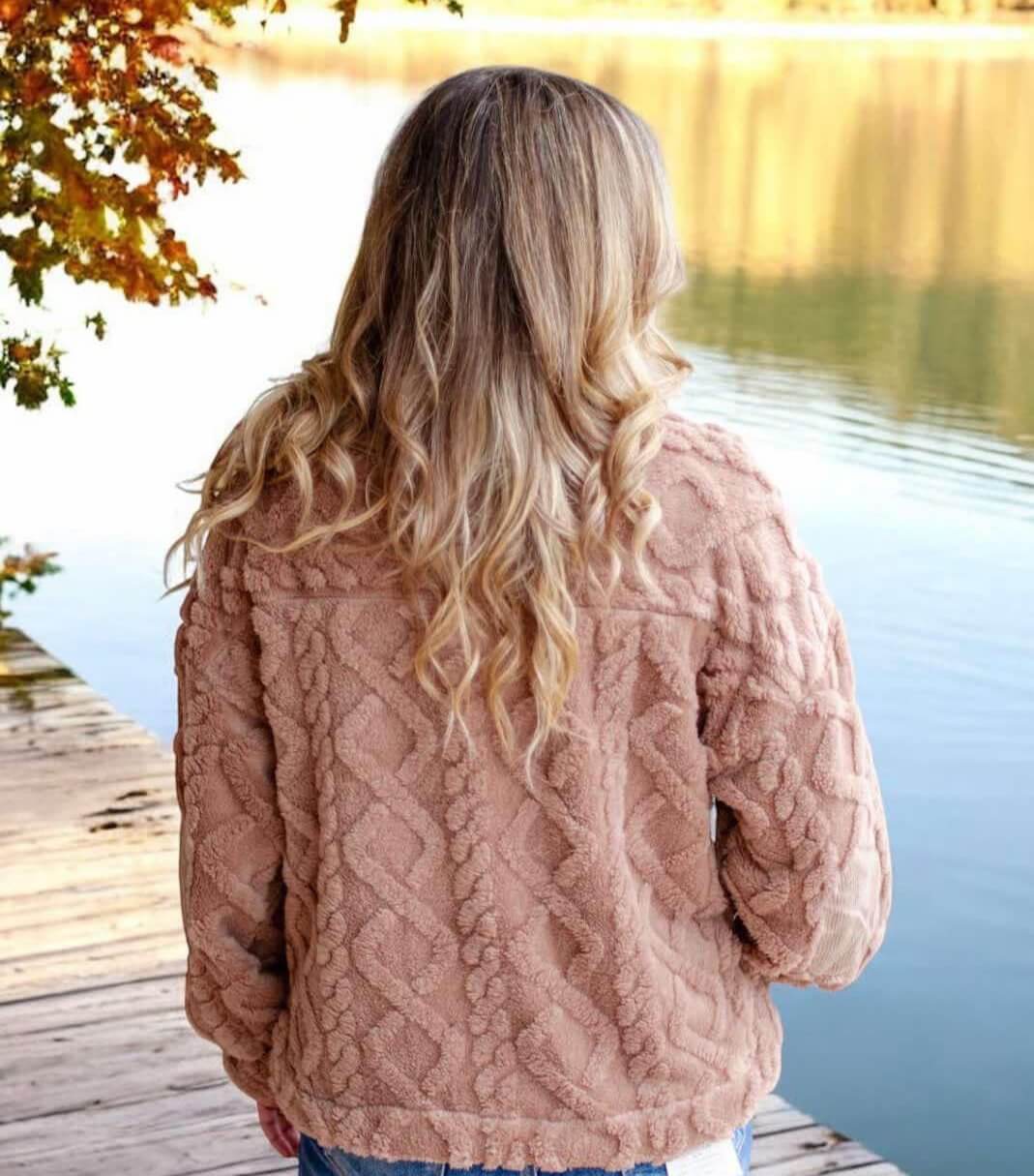 Woman wearing mocha teddy bear sherpa fleece pullover with cable pattern by lakeside in fall scenery.