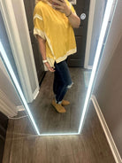 Woman in mellow yellow top with white accents and ripped jeans, posing in front of a full-length mirror.