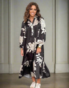 Woman wearing LOOKING UP Dress by Umgee with black and white floral pattern, hi/low hem, long sleeves, and tiered ruffle.