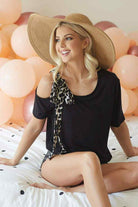 Model wearing Feline Fancy Top, black tee with leopard print bow, styled with a wide-brim hat against pastel balloons.