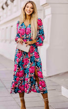 Woman in floral PERFECT POISE DRESS with V-neck and balloon sleeves, showcasing a stylish summer look with a slit and accessories.