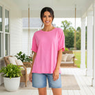 Woman wearing FEEL GOOD FAVE TOP - Andree' (pink) with shorts, standing on a porch with greenery.