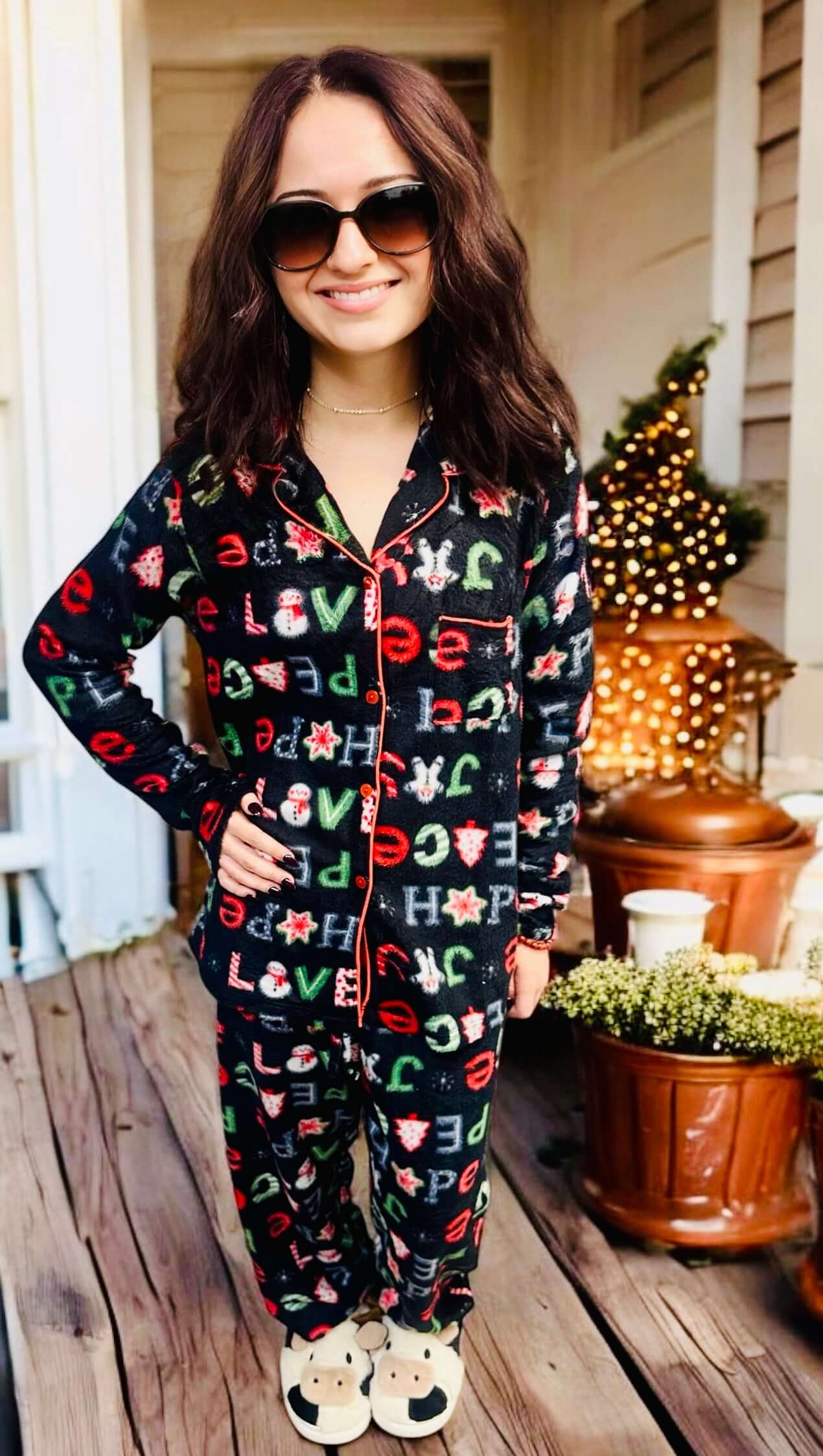 Woman wearing Peace Love Hope PJs by Love To Sleep, featuring Christmas designs and red trim, standing on a porch.