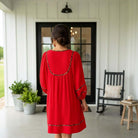 Woman wearing a RED HOT CONFIDENCE DRESS with pockets, standing in a cozy outdoor setting.