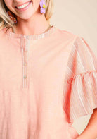 Close-up of Ruffled Breeze cotton top in peach with ruffle sleeves and button details, styled for chic outfits.